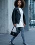 Woman walking on a city street wearing a black leather jacket, white shirt, blu and black tights, and high heels.