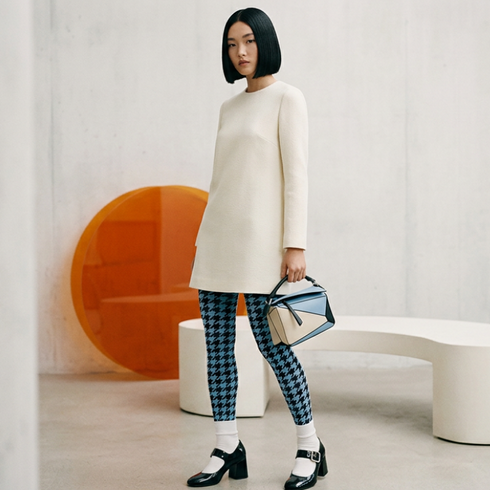 Woman in a white mod dress and houndstooth tights standing in a modern interior setting.