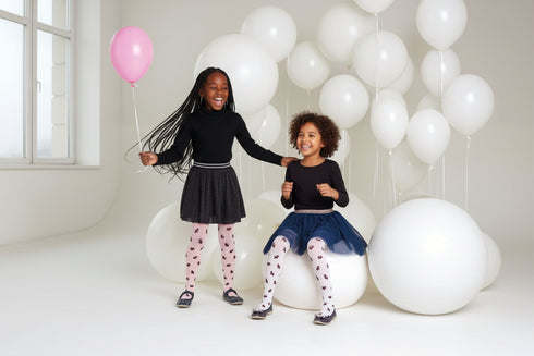 Two young girls standing together with balloons and white balloons in the background