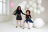 Two young girls standing together with balloons and white balloons in the background