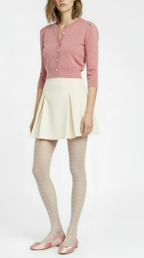 Woman wearing a pink cardigan, cream skirt, and white tights on a white background