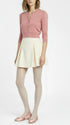 Woman wearing a pink cardigan, cream skirt, and white tights on a white background