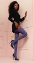 Woman wearing a black outfit with blue stockings against a white wall.