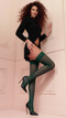 Woman wearing a black outfit and green stockings against a light-colored wall.
