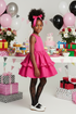Young girl in a pink dress and black star tights with colorful balloons and flowers in the background