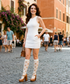 Woman in a white dress and polka dot knee-high socks standing on a cobblestone street.
