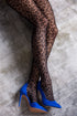 Leopard print tights worn with blue high-heeled shoes on a textured surface