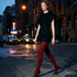Woman walking on a city street at night with neon signs in the background black dress and black and red houndstooth tights