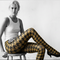 Woman wearing a white tank top and patterned tights sitting on a stool against a white background.