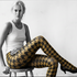 Woman wearing a white tank top and patterned tights sitting on a stool against a white background.