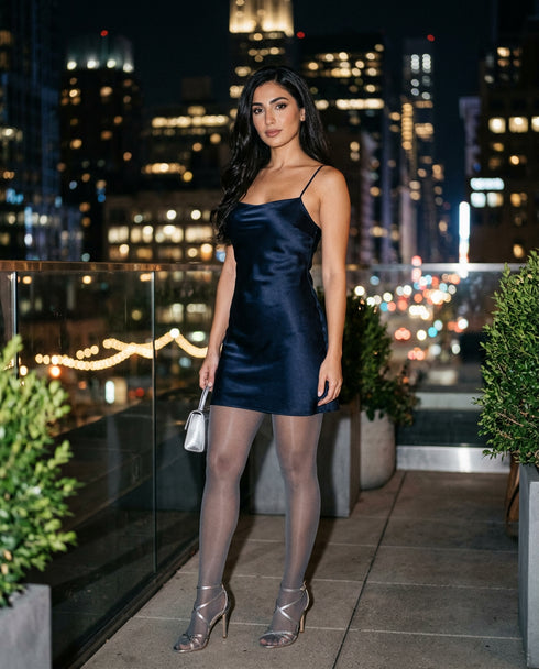 Woman in a navy blue dress standing on a rooftop with city lights in the background