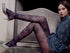 Woman wearing floral-patterned tights and denim shorts sitting on a chair.