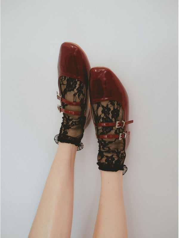 Red shoes with lace details worn by a person on a plain background