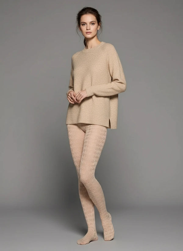 Person wearing a beige cable knit sweater sitting on a light gray surface with a neutral background
