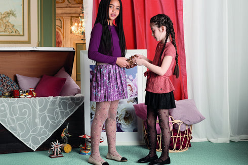 Two young girls in a room with a red curtain and decorative items. wearing floral patterned tights