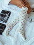 White knee-high socks with brown polka dots worn by a person on a white surface.