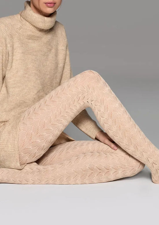 Person wearing a beige cable knit sweater and pants on a gray background