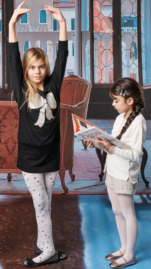 Two young girls in a staged indoor setting with a decorative background wearing cute tights.